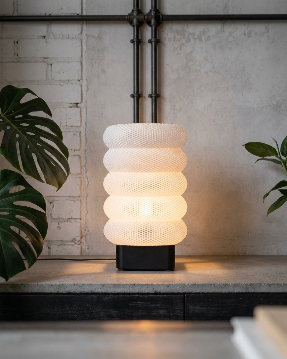 Luméa Arch table lamp with a black base, lit, on a concrete shelf
