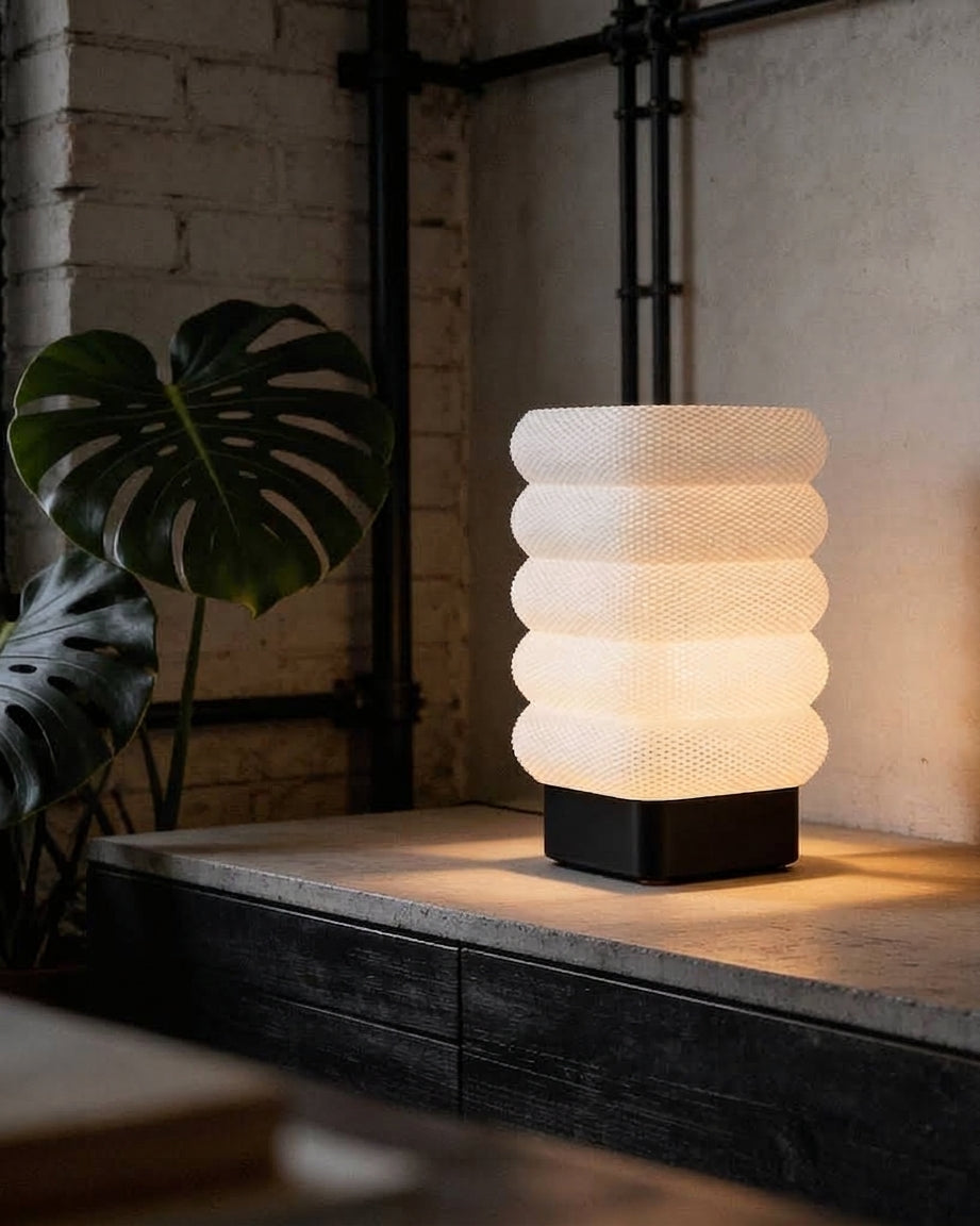 Luméa Arch table lamp with a black base, side view against brick